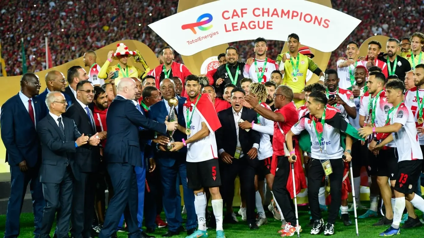 Le patron de la FIFA en train de passer la coupe de la TotalEnergies CAF Champions League à Yahya Jabrane, capitaine du Wydad, pendant que les autres joueurs sautent de joie derrière eux - SNRTNews